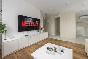 A modern living room with a flat-screen TV displaying the Netflix logo, a white entertainment unit, a coffee table with magazines, and a plant. - Lumina 3 room Apart near Pałac Kultury (Warszawa)