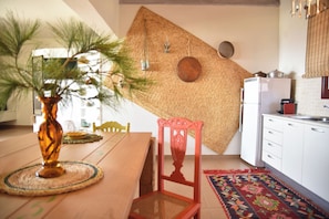 A kitchen with a wooden table, a red chair, and a woven wall hanging. - Elefthia Syros-Luxury Houses & Suites (Syros)