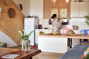 A kitchen with a central island, a refrigerator, and a window with blinds. - Elefthia Syros-Luxury Houses & Suites (Syros)