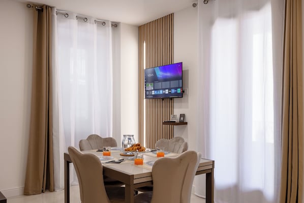 Et moderne spiseområde med et fladskærms-tv på væggen, et spisebord med stole og et morgenmåltid med croissanter og appelsinjuice.