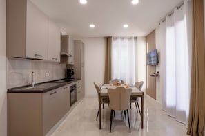 Une cuisine moderne avec un coin repas, un téléviseur à écran plat fixé au mur et un coin petit-déjeuner avec des croissants et du jus d’orange.