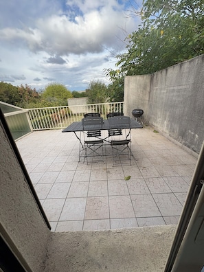 An outdoor patio with a table and chairs, a barbecue grill, and a view of the surrounding greenery.