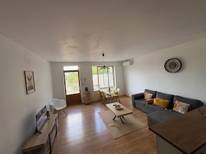 A living room with a sofa, a coffee table, a TV, and a dining area with chairs and a table.