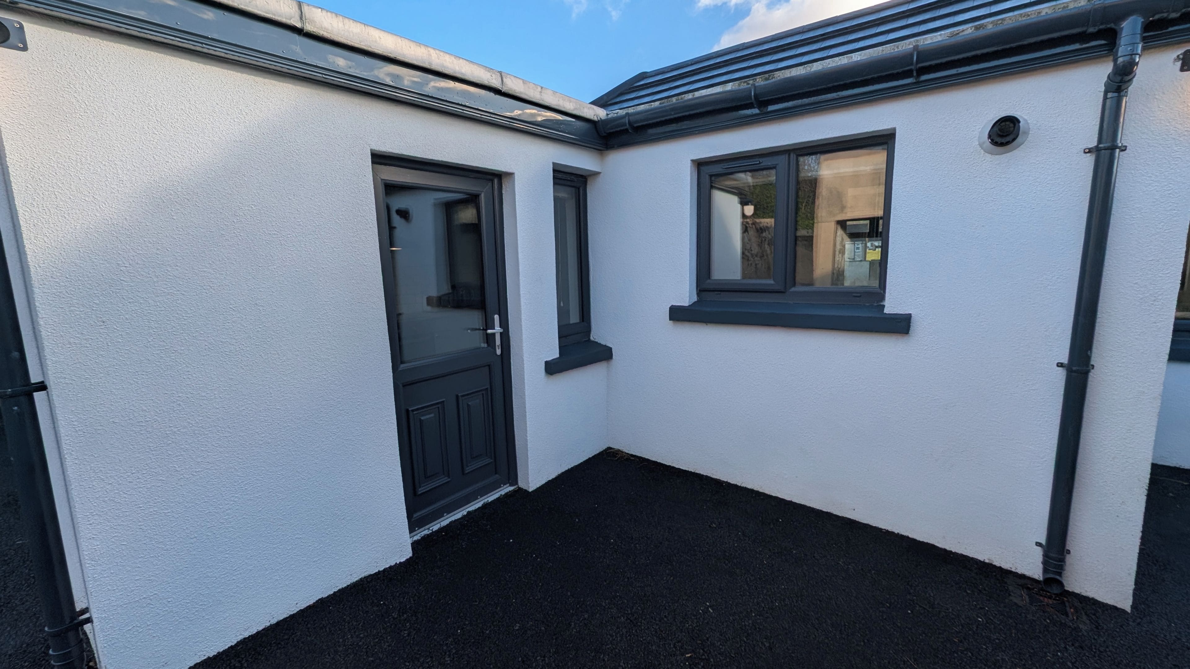 A corner of a building with a white exterior, a black door, and a window with a black frame.