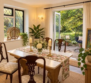 Ein Essbereich mit einem Tisch, gedeckt für vier Personen, umgeben von Stühlen und mit Blick auf einen Garten durch eine Glastür.