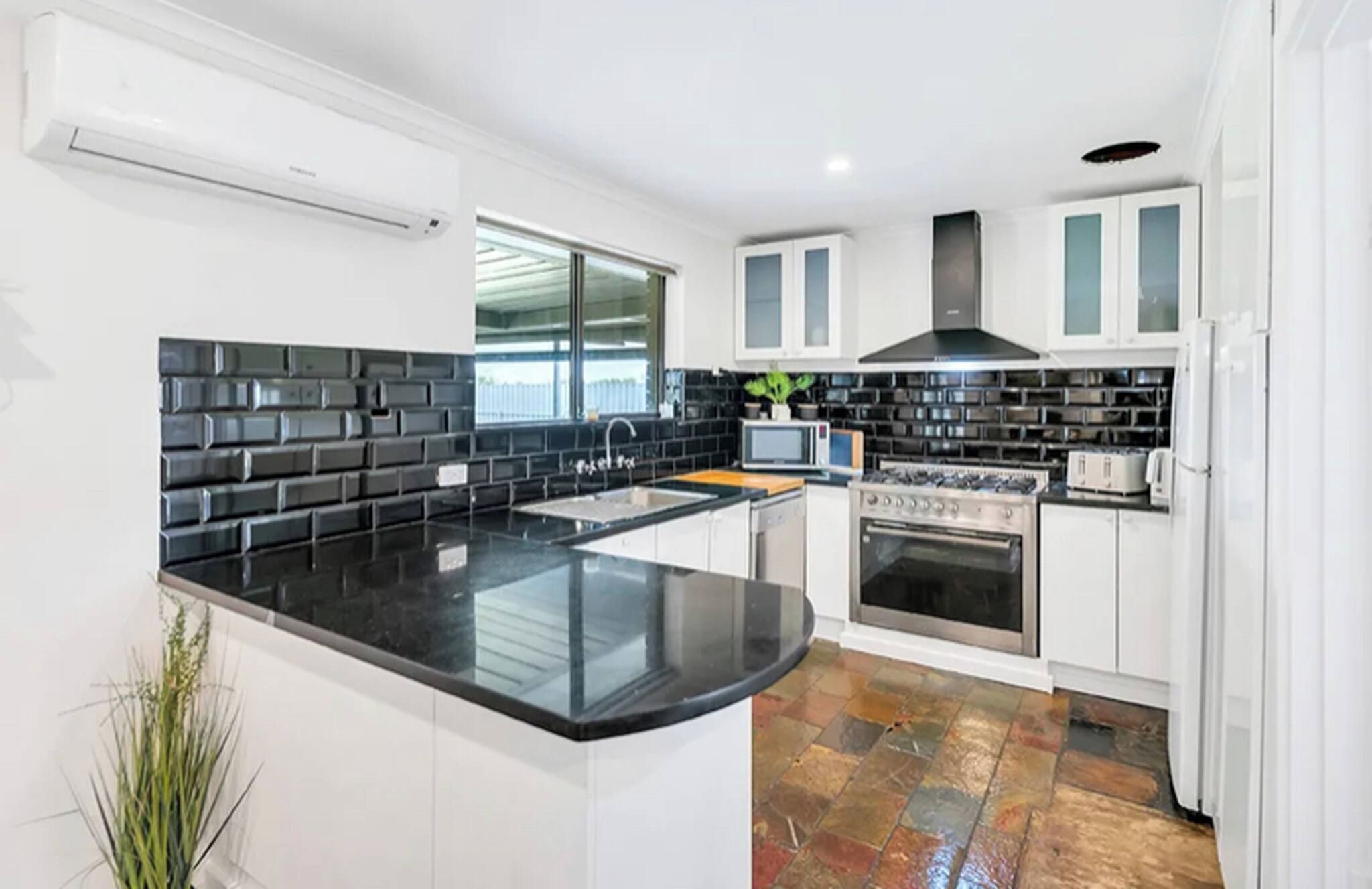 A modern kitchen with a black countertop, white cabinets, a stove, and a microwave.