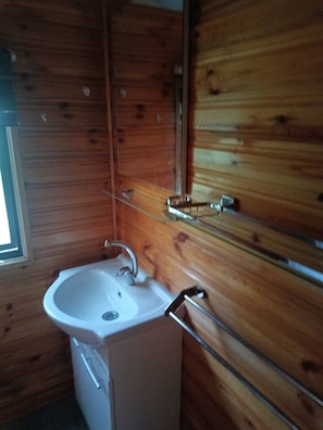 A wooden cabin interior with a white sink, wooden walls, and a window. - Gezinsvakantie in de Drentse natuur | Stacaravan (Wijster)