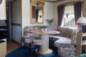 A compact living space with a sofa, a small round table, a television, and a mirror. - Gezinsvakantie in de Drentse natuur | Stacaravan (Wijster)