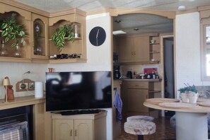 A compact kitchen with a flat-screen TV, wooden cabinets, and a clock on the wall. - Gezinsvakantie in de Drentse natuur | Stacaravan (Wijster)
