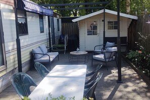 A covered patio area with a table and chairs, a small shed, and a mobile home. - Gezinsvakantie in de Drentse natuur | Stacaravan (Wijster)