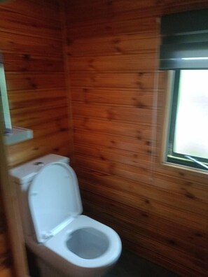 A small, wooden-paneled bathroom with a white toilet and a window. - Gezinsvakantie in de Drentse natuur | Stacaravan (Wijster)