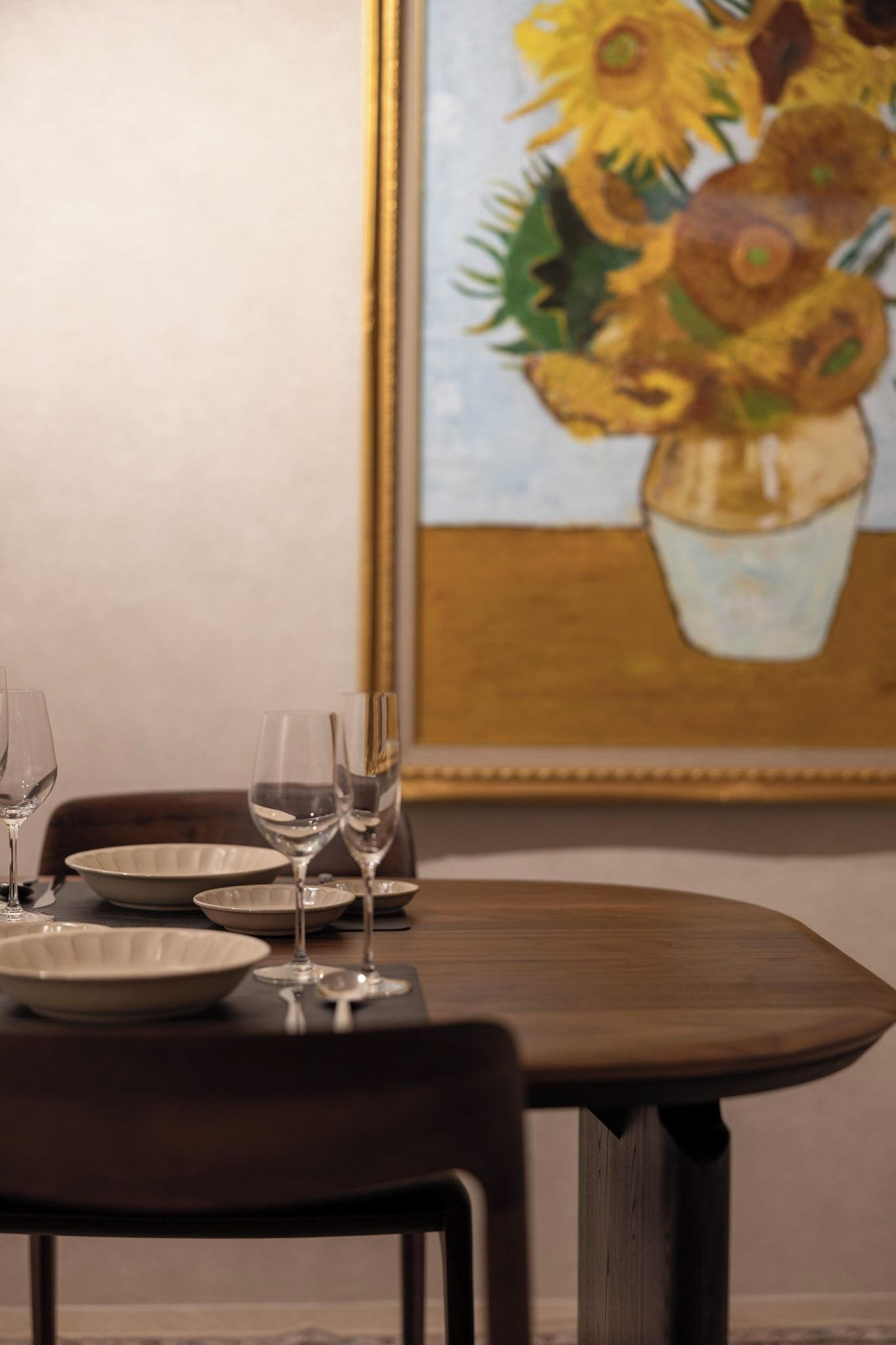 A dining table with plates and glasses, a chair, and a painting of sunflowers on the wall.