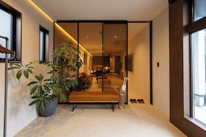 Un interior moderno con una zona de estar, una planta grande en maceta y un zapatero.