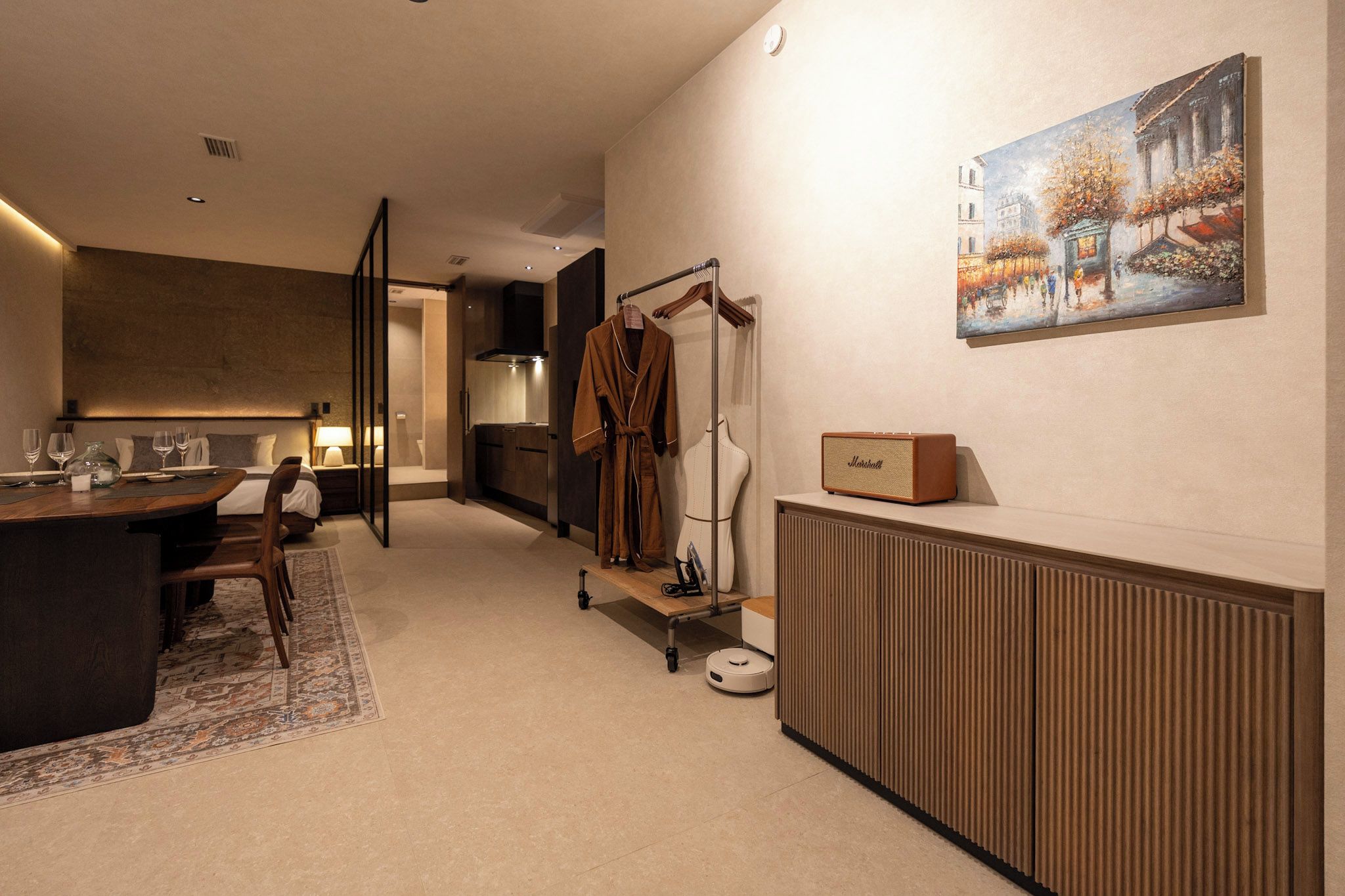 A modern hotel room with a dining area, a robe rack, a radiator, and a painting on the wall.