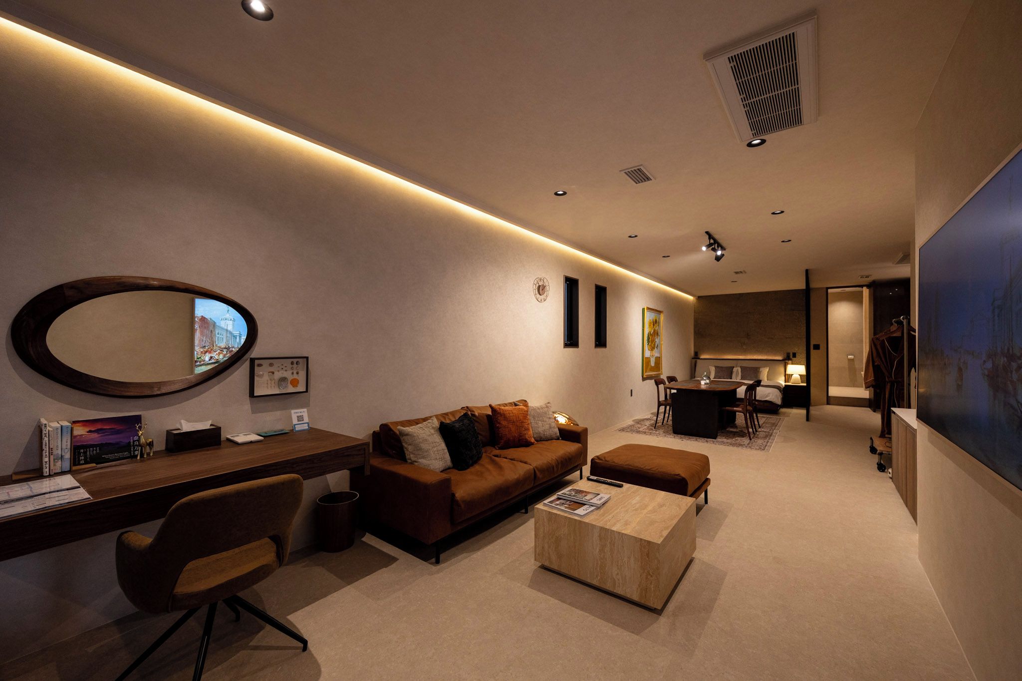 A modern hotel room with a desk, sofa, and a large mirror.