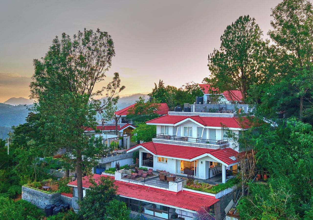 A multi-story residential building with a red-tiled roof, surrounded by lush greenery and overlooking a mountainous landscape.