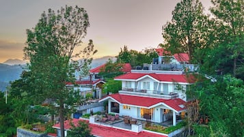 A multi-story residential building with a red-tiled roof, surrounded by lush greenery and overlooking a mountainous landscape.