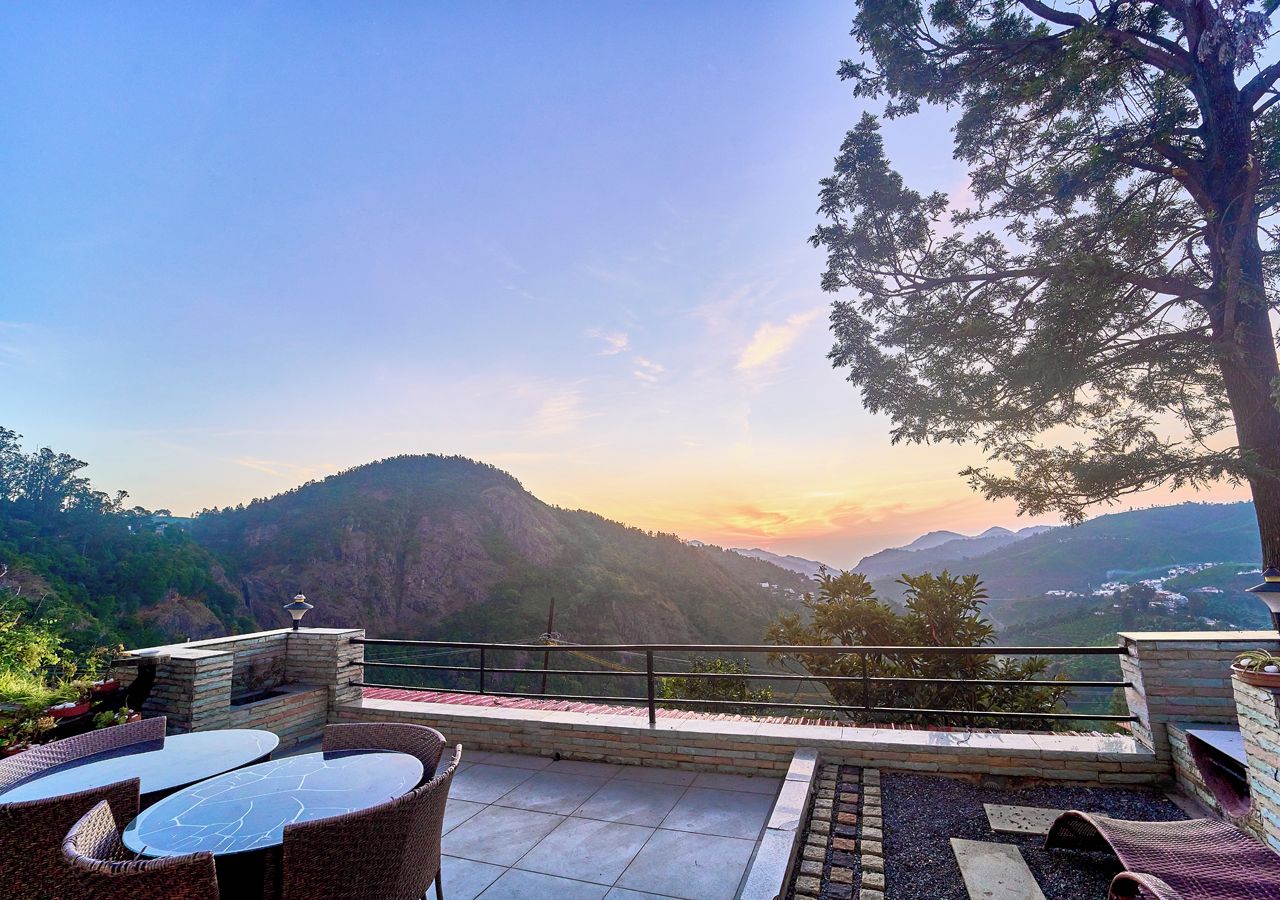 A terrace with a view of a mountainous landscape, outdoor seating, and a railing.
