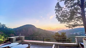 A terrace with a view of a mountainous landscape, outdoor seating, and a railing.