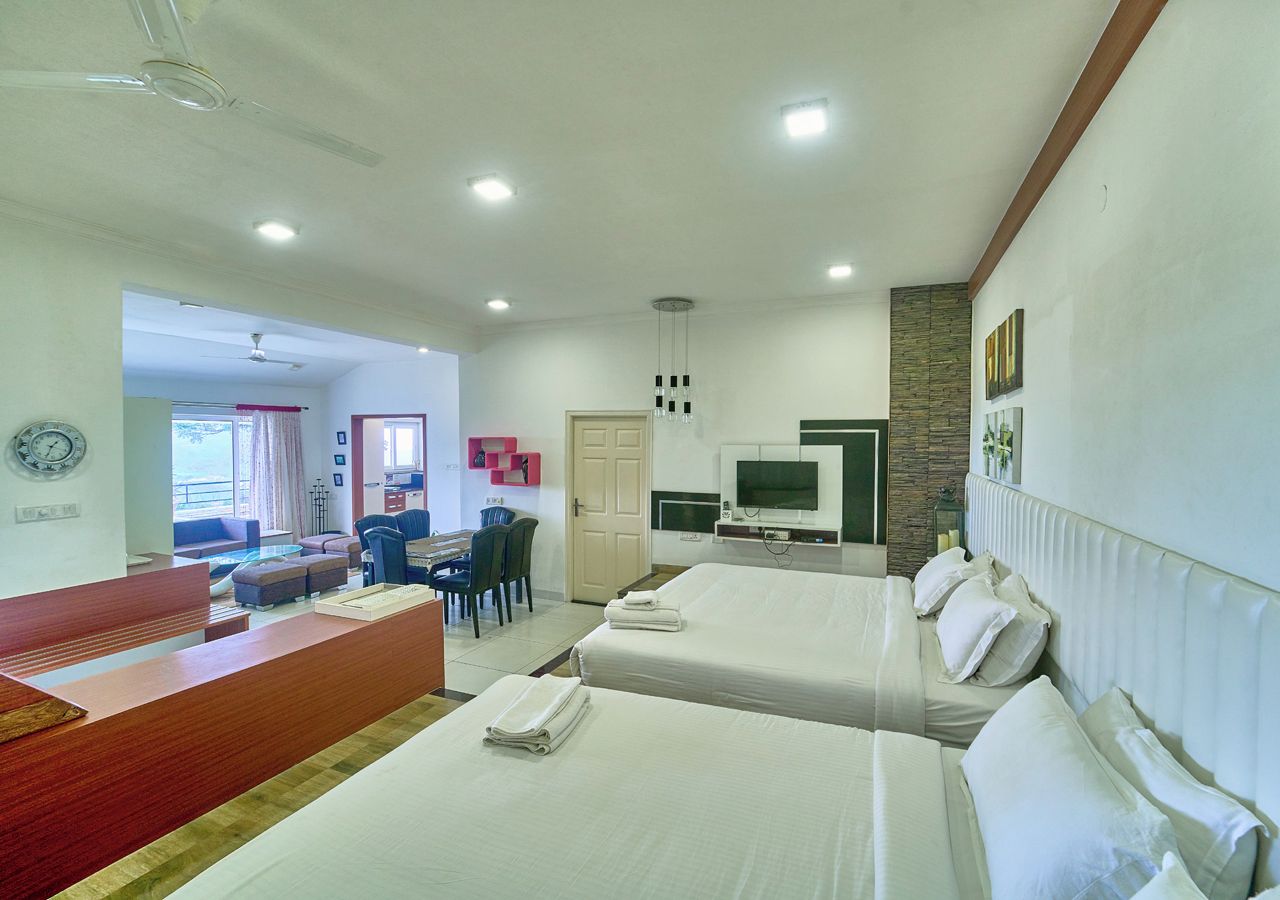 A hotel room with two beds, a desk, a television, and a view of the outside.