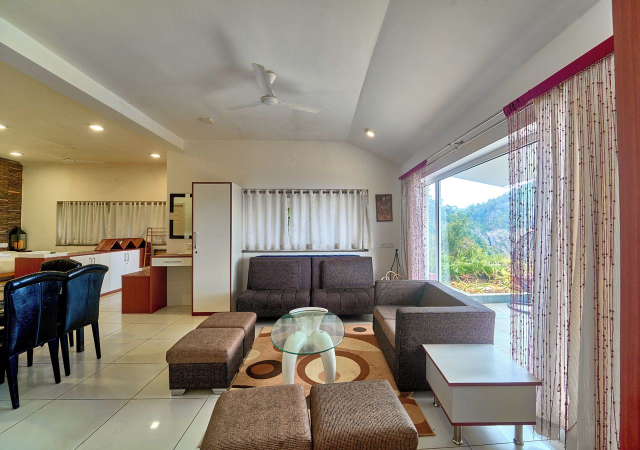 A modern living room with a sofa, ottomans, a glass coffee table, and a dining area with chairs and a table.