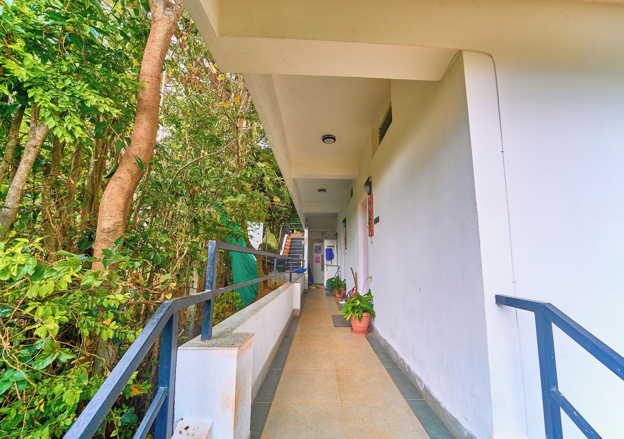 A corridor with a railing, potted plants, and a staircase leading to an upper level.
