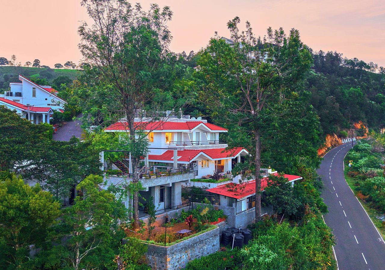 A multi-story residential building with a red roof, surrounded by lush greenery and a curving road.