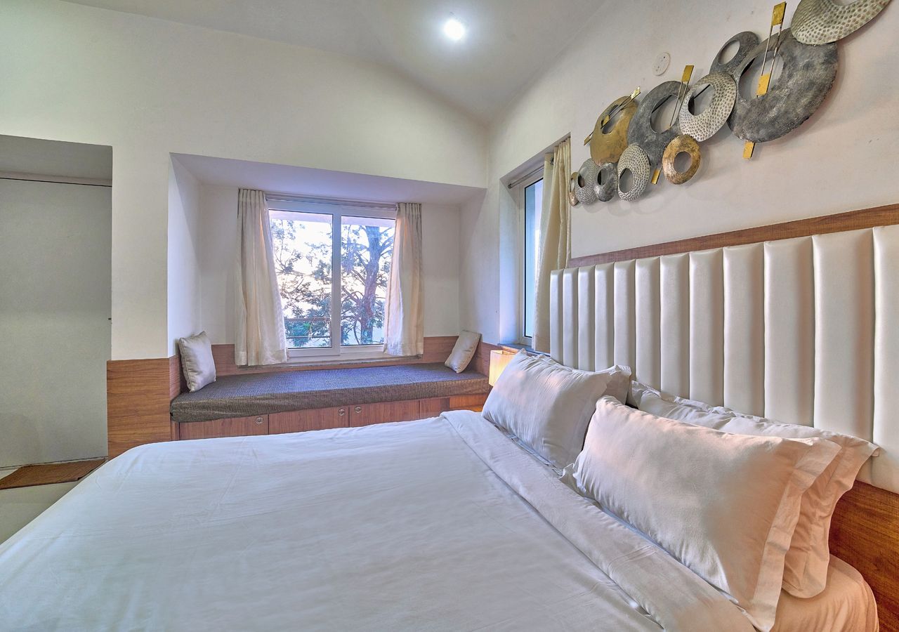 A bedroom with a large bed, a window seat, and a decorative wall piece.