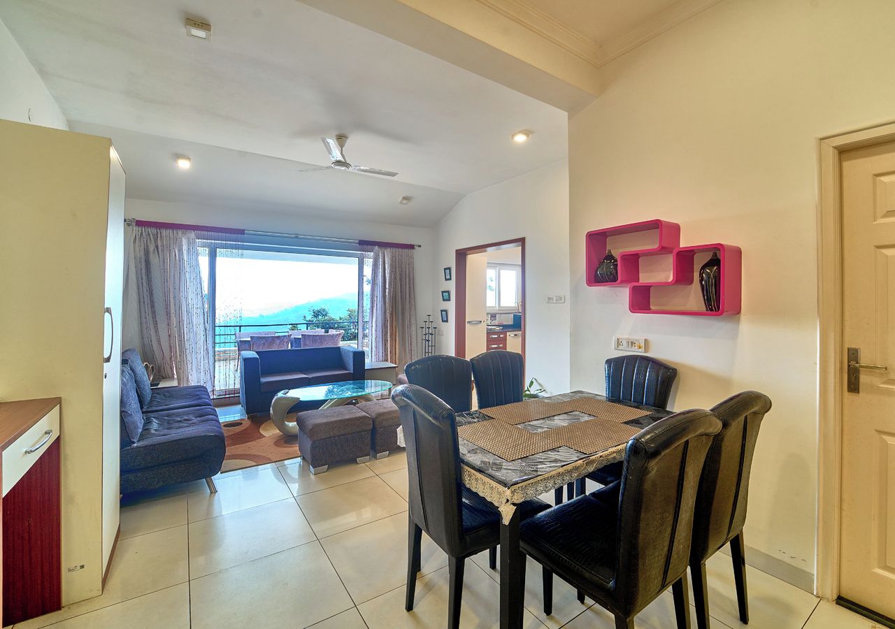 A modern living room with a dining area, a sofa set, and a view through a large window.