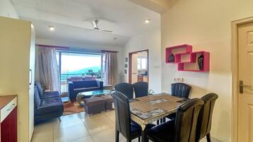 A modern living room with a dining area, a sofa set, and a view through a large window.
