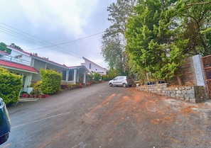 A residential street with houses, a parked car, and a stone wall. - Cozy Retreat Inn Ooty by VOYE HOMES (Coonoor)