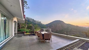 Una terrazza con tavolo e sedie, circondata da piante e affacciata su un paesaggio collinare.