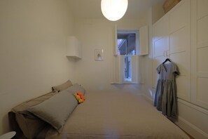 Een slaapkamer met een bed, kussens, een hangende jurk en een kledingkast.