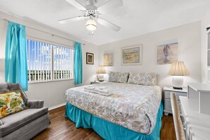 Ein Schlafzimmer mit einem Bett, einem Sessel, einem Deckenventilator und einem Fenster mit Vorhängen.