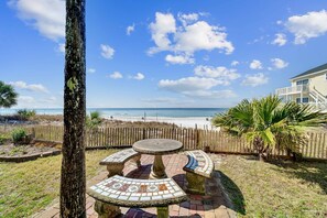 Eine Terrasse mit einem runden Tisch und Bänken, einem Holzzaun und Blick auf den Strand.