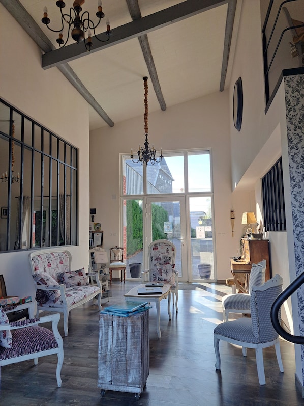 Una habitación amplia con techo alto, un candelabro y un gran ventanal con vistas al exterior.