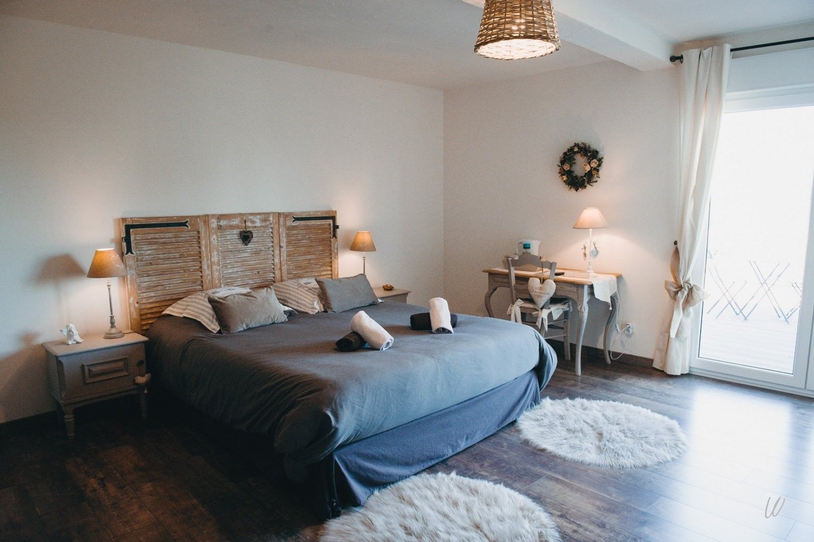 Une chambre à coucher avec un grand lit, deux tables de chevet, un bureau, une chaise et une fenêtre avec des rideaux.