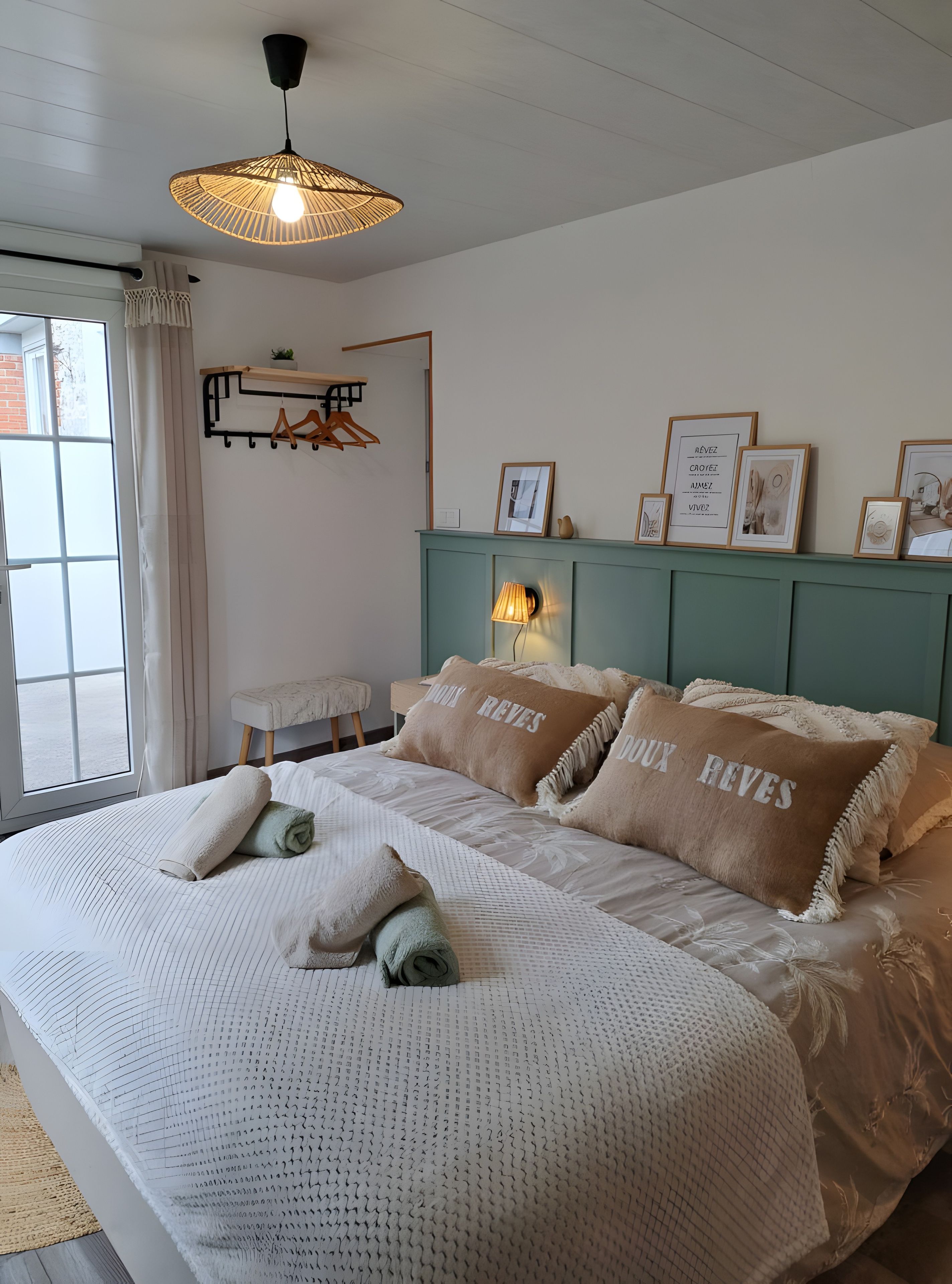 Een slaapkamer met een groot bed, een hanglamp, een nachtkastje en een wandplank met ingekaderde foto's.