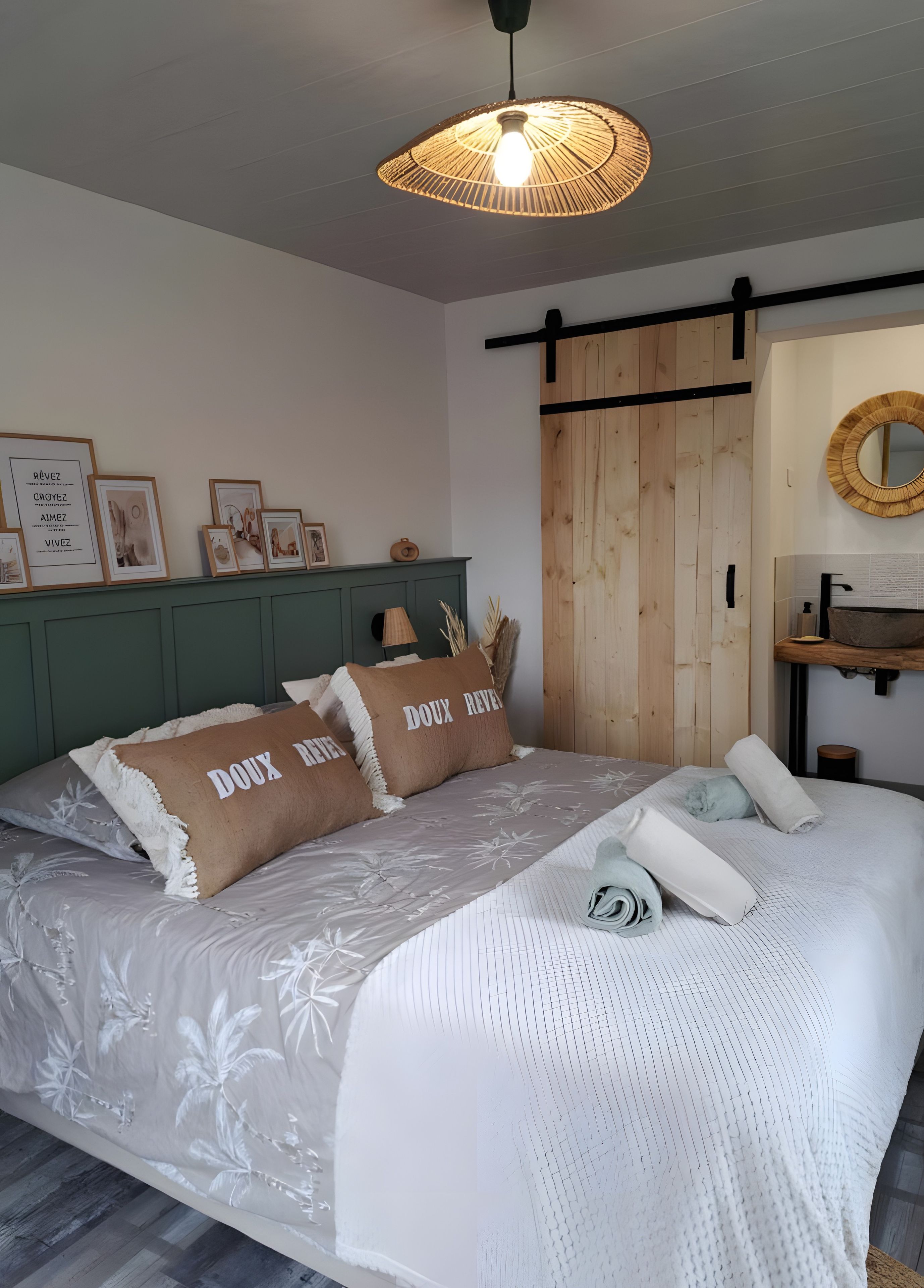 Een slaapkamer met een bed, een hanglamp, een houten deur, een spiegel en ingelijste foto's aan de muur.