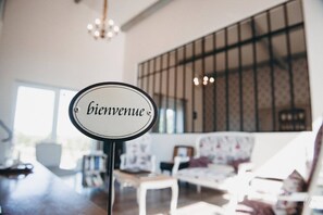 Un cartel con la palabra 'bienvenue' en una habitación con un ventanal grande, una araña y un sofá.