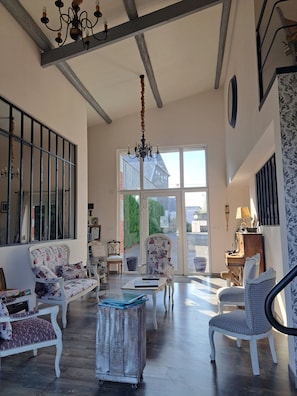 A spacious room with a high ceiling, a chandelier, and a large window offering a view of the outside. - Bed and Breakfast 'Chambres Azélice' with Shared Terrace, Shared Garden and Wi-Fi (Féron)