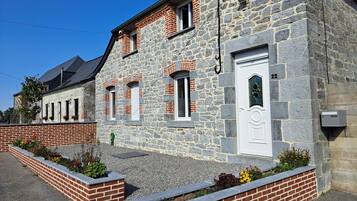 Un bâtiment en pierre avec une porte blanche, portant le numéro 22, et un petit jardin agrémenté de parterres de fleurs.