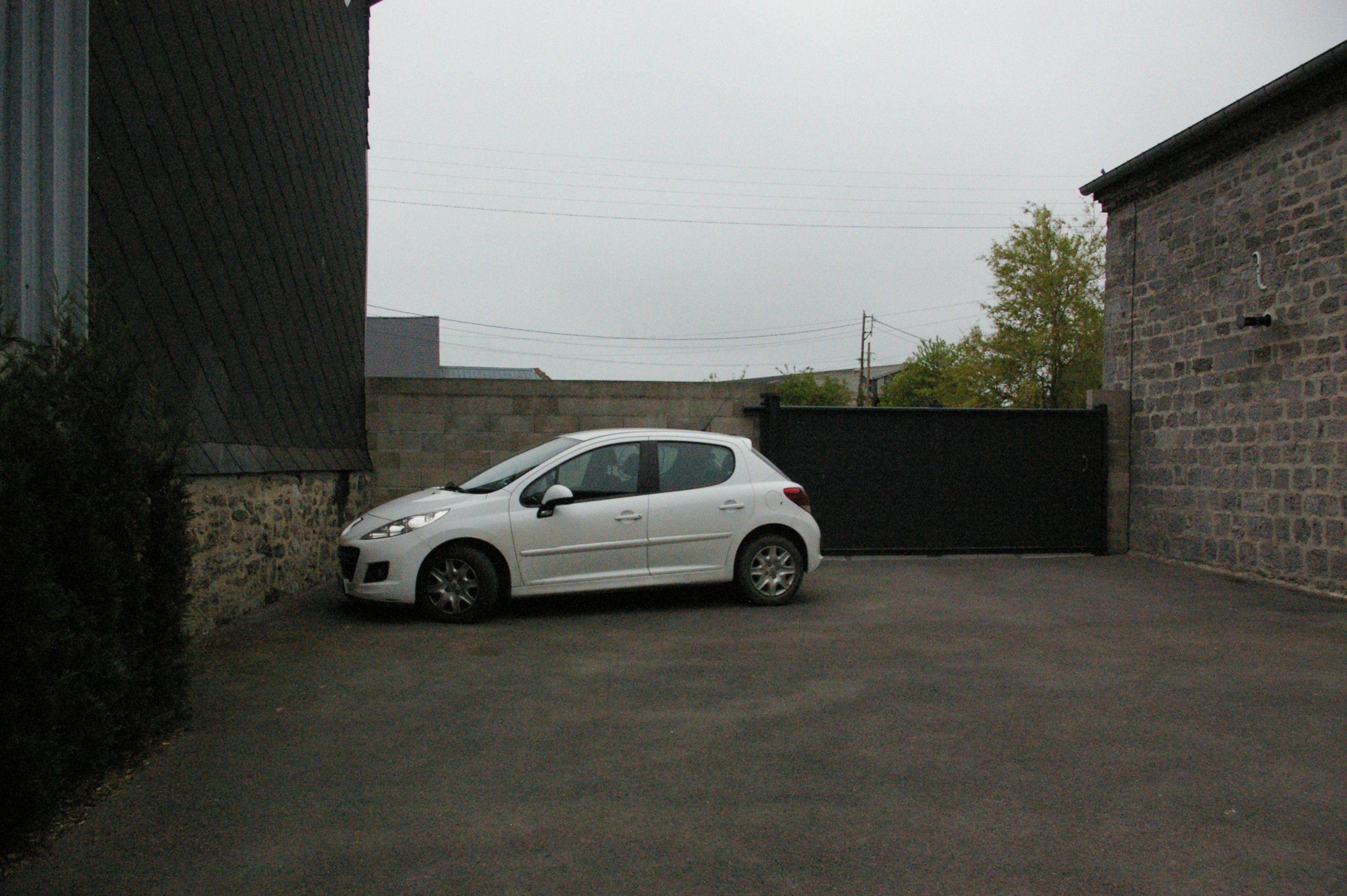 A white car parked in a paved area with a brick wall and a metal gate in the background.
