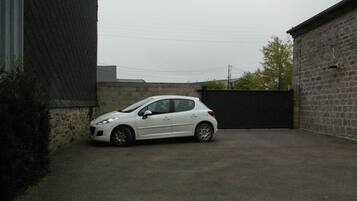 A white car parked in a paved area with a brick wall and a metal gate in the background.