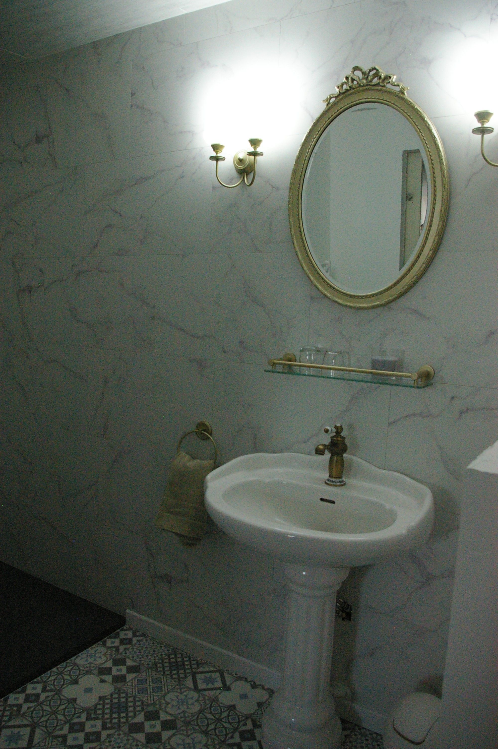 Une salle de bain avec un lavabo blanc, un miroir et un luminaire fixé au mur.