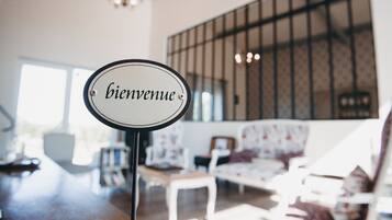 Een 'bienvenue'-bord in een kamer met een groot raam, een kroonluchter en een gestreept sofa.