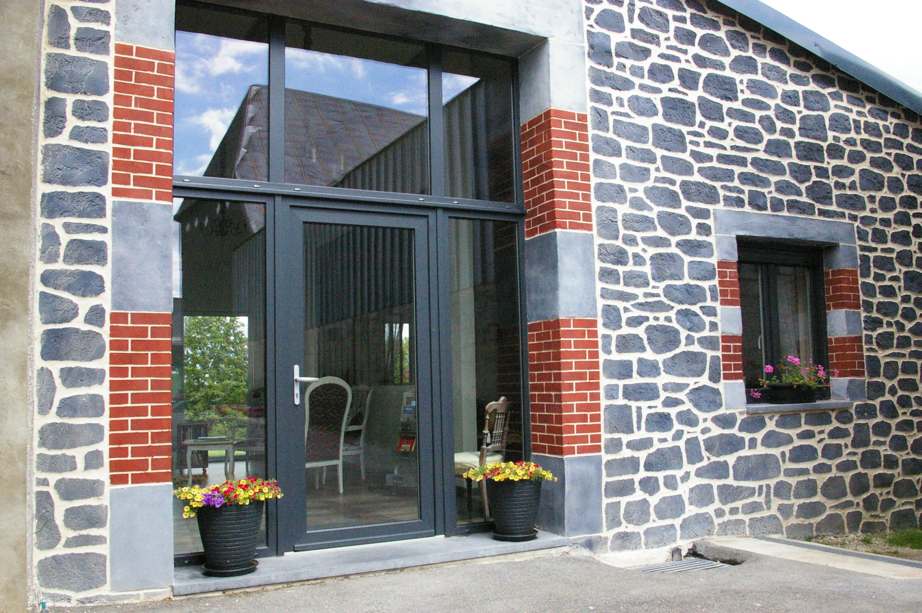 A building with a stone facade, large glass doors, and potted plants on the ground level.