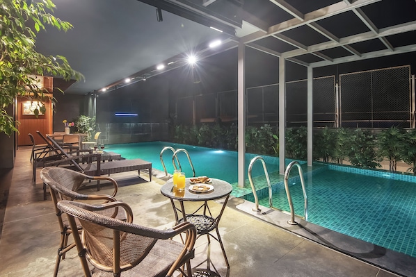Un área de piscina al aire libre con sillones de descanso y una mesa, rodeada por un porche cubierto.