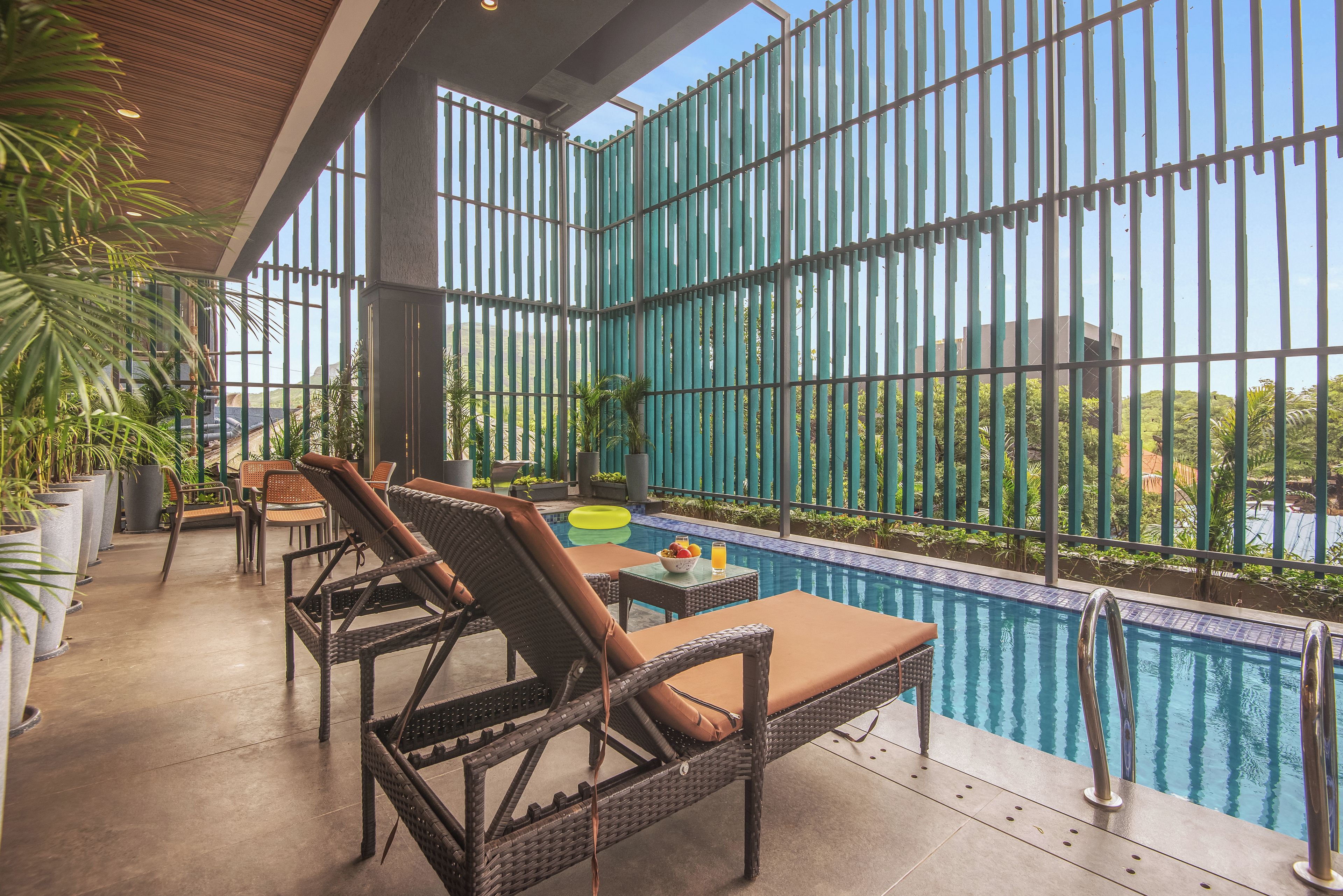 Zona junto a la piscina con sillones de mimbre y una mesa, rodeada por una valla metálica.