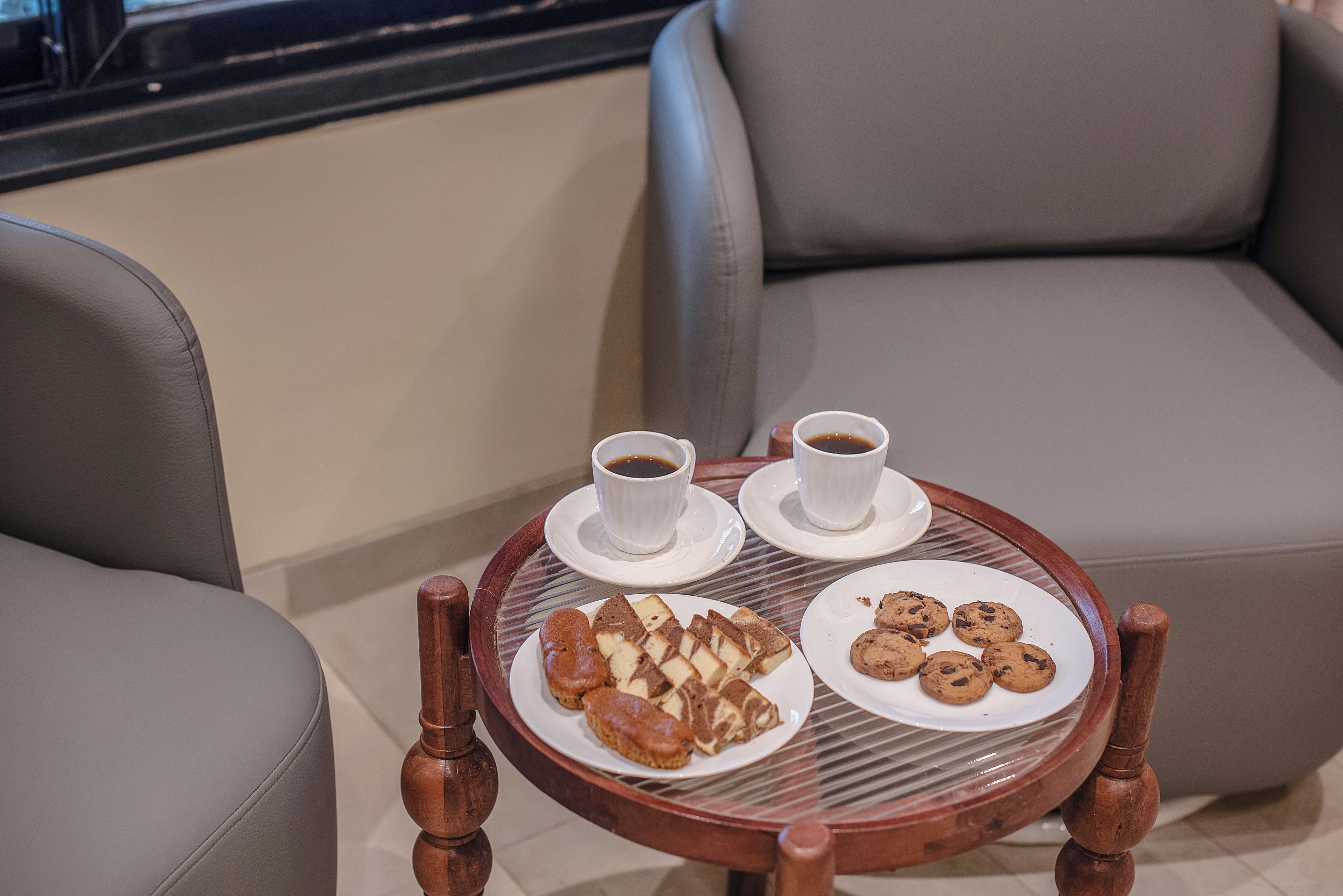 A round wooden table with two white cups of coffee and a plate of cookies.